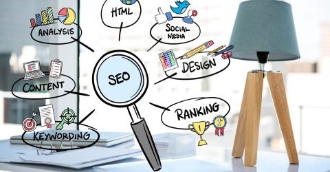 "SEO concept illustration with a magnifying glass surrounded by hand-drawn icons for analysis, HTML, social media, design, ranking, content, and keywording, on an office desk with a wooden tripod lamp